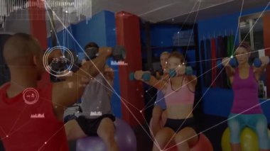 Eğitmen, denge topları üzerinde dambıl kaldıran müşterilere sinyal veriyor. Kişisel eğitim, grup çalışması, dijital fitness, kuvvet eğitimi, fonksiyonel fitness, spor salonu ortamı, spor kıyafeti