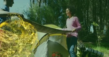 Yetişkin bir kadın ekose battaniyeyi sallıyor, adam altın kıvılcımlar gibi kenarda kıvrılıp kamp ateşi arıyor. Macera, açık hava, doğa, köy, konfor, arkadaşlık, rahatlama