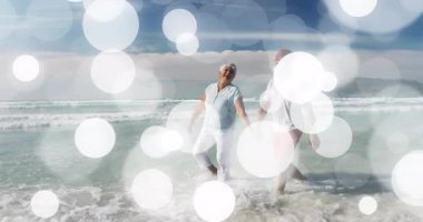 Romantik çift el ele tutuşup sığ dalgalara atlıyor, seyahat reklamı için ayaklarını dalgaların altına sokuyor. Bağlantı, arkadaşlık, deniz kenarı, rahatlık, dinginlik, birliktelik, seyahat