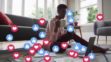 Kadın kupayı yudumluyor dizüstü bilgisayarını inceliyor, sosyal medya simgeleri ekranda dolanıyor ve bağlılığını gösteriyor. İçerik oluşturucu, uzaktan çalışma, dijital iletişim, sosyal medya, ev ofisi, teknoloji, yaşam tarzı