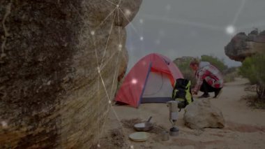 Erkek kampçı kamp alanına giriyor ve kahve demlemek için taşınabilir sobayı düz kayanın üzerine monte ediyor. Macera, vahşi doğa, açık hava, keşif, engebeli yaşam tarzı, ekipman