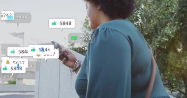 Şehir meydanında yürüyen bir kadın akıllı telefona bakıyor ve sosyal bildirimleri kontrol ediyor. Akıllı telefon, dijital, bağlantı, şehir, yaşam tarzı, modern, canlı