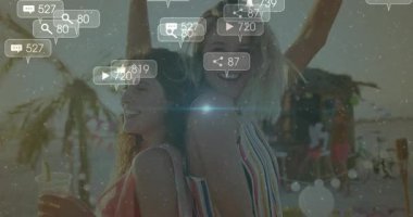 Gün batımında plaj partisinde dans eden iki kadın, nişan için sosyal medya simgeleri etrafında yükseliyor. Kutlama, dostluk, gece hayatı, açık hava, canlı, enerji, boş zaman