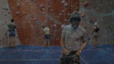 Climbing partners approaching wall, adjusting harness for climb while network overlay tech pulsing. Adventure, teamwork, fitness, preparation, motivation, athleticism, sport