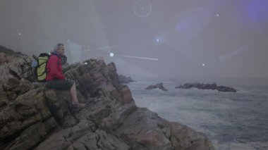 Uçurumda oturan erkek yürüyüşçü teknolojiyi kullanarak ışıldayan canlı veri hatlarını haritalandırıyor. Macera, keşif, yenilik, doğa, bağlantı, teknoloji, vahşi yaşam