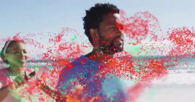 Kumsalda kucaklaşan bir çift, telefon kaldıran, dönen parçacıklar olarak tablet görüntüleme teknolojisini izliyorlar. Romantik, dijital, bağlantı, kutlama, canlı, açık hava, mutluluk