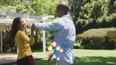 Çift pergola altında el ele tutuşarak, sosyal medya tepki simgeleri üreterek selamlıyor. Sevgi, kutlama, yakınlık, bağlantı, arkadaşlık, açık hava, neşe