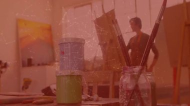 Erkek sanatçı boya kavanozları arasında yaratıcı bir vizyon arayarak tuvalin önünde durarak stüdyoya giriyor. Yaratıcı, içe dönük, minimalist, ilham verici, sanatsal, sakin, profesyonel