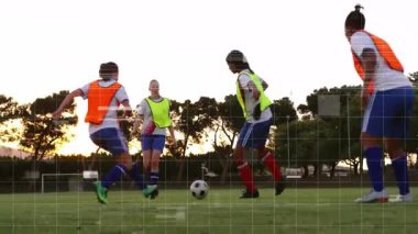 Futbol antrenmanında yuvarlanan topu kovalayan dört bayan oyuncu gün batımında yükselen slayt müdahalelerini gerçekleştiriyor. Atletizm, takım çalışması, egzersiz, açık hava, coşku, kararlılık, spor