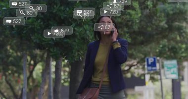 Orta yaşlı bir kadın kaldırımda yürürken akıllı telefondan konuşuyor, sosyal bildirimler etrafında beliriyor. Kentsel, teknoloji, iletişim, dijital, yaşam tarzı, modern, bağlantı