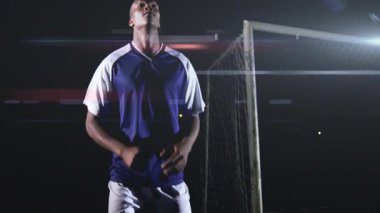 Futbol defans oyuncusu spot ışıkları altında topun yerini değiştiriyor ve takip ediyor. Rakip başlığı engelliyor. Atletizm, rekabet, atletizm, gece vakti, spor, eylem, yoğunluk