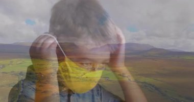 Çocuk parlak sarı maskeyi yüze doğru kaldırıyor ve sağlık koruması için elastik halkalar takıyor. Gençlik, açık hava, koruma, güvenlik, esneklik, doğa, sükunet