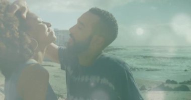 Çift plaj öpücüğünü paylaşıyor. Kırmızı saç tokası ve sürüklenen mercek fişekleri pazarlama için kullanılıyor. Romantizm, şefkat, yakınlık, bağlantı, açık hava, yaşam tarzı, canlı