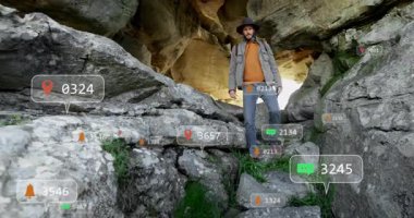 Erkek kaşif kayalık mağara çıkıntısında duruyor, teknik demo sırasında yüzen bildirim simgeleri başlatılıyor. Macera, keşif, dijital, teknoloji, açık hava, engebeli, keşif