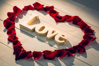 Tahtada kırmızı gül yaprakları olan kalp şeklinde bir çerçeve.