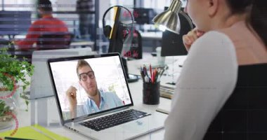 Ofis çalışanı, dizüstü bilgisayarın etrafında beliren finans tablolarını inceleyerek iş arkadaşını selamlıyor. İşbirliği, teknoloji, veri görselleştirme, çalışma alanı, profesyonel iletişim, modern