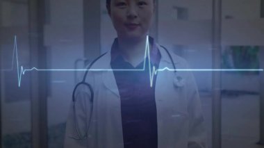 Kadın doktor gülümseyerek tepki verirken EKG dalgası klinik koridorunda kayarak tedaviyi işaret ediyor. Tıbbi, sağlık, profesyonellik, teknoloji, tanı, klinik, sağlık