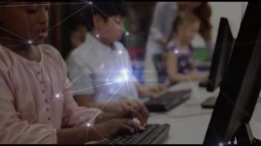 Öğretmen klavyeye eğiliyor ve bilgisayar laboratuvarında daktilo eden öğrencilere monitörü işaret ediyor. İşbirliği, akıl hocalığı, eğitim, teknoloji, odaklanma, rehberlik, çeşitlilik