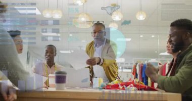 Sunucu ayakta ve tabloları yayıyor. Masanın üzerindeki kumaş örnekleri tasarım ölçülerini gösteriyor. İşbirliği, takım çalışması, yenilik, yaratıcı, profesyonel, veri görselleştirme, tekstil