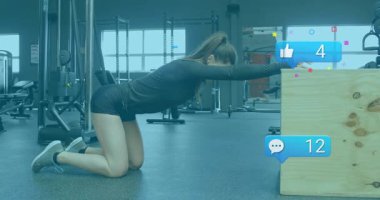 Kadın diz çöküp ellerini kutuya koyuyor spor salonunda omuzlarını geriyor ve hareketli sosyal simgeler yükseliyor. Fitness, power, mobility, wellness, modern, enerjik, egzersiz