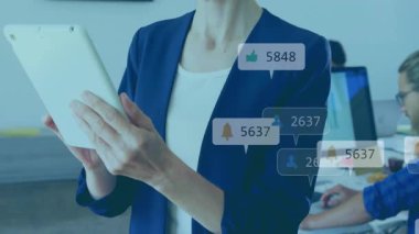 Masa başı ekranında elinde tablet tutan kadın, yükselen sosyal istatistikleri izleyen yüzen simgeleri gösteriyor. Analizler, üretkenlik, teknoloji, iş, veri, yenilik, iletişim