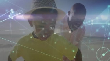 Babası çocuğun beline uzanıp, onu teknoloji kaplamalarıyla kumsalda eğlenceli bir şekilde tutuyordu. Aile, kaynaşma, kıyı, eğlence, canlı, neşeli, açık hava.