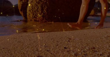 Gün batımında yosunlu kayanın yanında yürüyen bir adam suya dokunarak dalgalanmalar yaratıyor. Kıyı, sükunet, dinginlik, yansıma, doğa, rahatlık, manzara