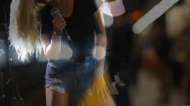 Düşük açılı çekim, sahne ışıkları altında mikrofon çalan kadın vokalisti gösteriyor. Performans, konser, eğlence, sahne, müzisyenler, canlı, enerji