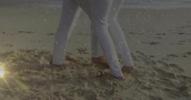 Dalgalara yakın kumlara basan ve seyahat pazarlaması için kalp ikonlarıyla plaj dansına başlayan çift. Romantizm, mahremiyet, deniz kenarı, yalınayak, gün batımı, bağlantı, sükunet