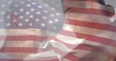 Amerikan bayrağını açan adam, vatansever kutlamaları paylaşan çiftler arasında dalgalanıyor. Vatanseverlik, birlik, açık hava, doğal aydınlatma, şefkat, kutlama, arkadaşlık