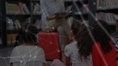 Eğitimci kırmızı kübün üzerinde oturuyor resim kitabını açıyor ve eğitim köşesindeki çocuklara hikaye okuyor. Öğrenme, okuma yazma, icat, merak, etkileşim, renkli, eğitici