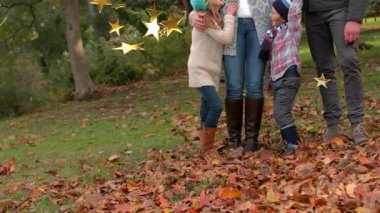 Kamera, ailenin yapraklara sarıldığını ve altın yıldızların markalaşmak için sürüklendiğini gösteriyor. Aile, sonbahar, doğa, kutlama, birliktelik, sıcaklık, açık hava.