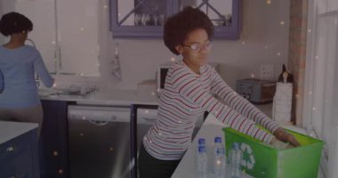 Genç kız mutfağa giriyor, yeşil geri dönüşüm kutusunu açıyor, kağıtları kabartıyor ve şişeleri yüklüyor. Çevre, ev, sürdürülebilirlik, takım çalışması, çevre dostu, aile içi, modern