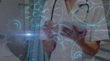 Kadın doktor tableti tıklatıyor ve holografik dişliler dönüşümlü olarak dönerken verileri araklıyor. Sağlık, teknoloji, yenilik, teletıp, veri, dijital, profesyonel