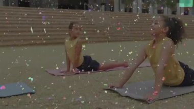 İki arkadaş çimenli plazada yoga minderlerine el sıkışıyor ve spor yapmak için kobra esnemesi yapıyorlar. Çocuklar, sağlık, açık hava, aktivite, arkadaşlık, rahatlama, doğal