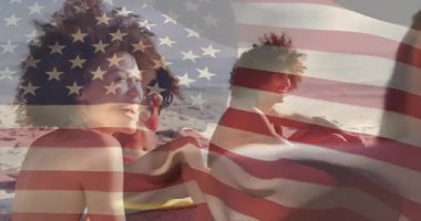 Arkadaşların suya yakın plaj havlularında oturup arkadaşlarıyla yolculuk anlarını paylaşmalarına tepki gösteriyorlar. Sahil, yoldaşlık, rahatlama, açık hava, güneşli, boş zaman, mutluluk.