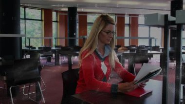 Kadın kütüphane masasına kırmızı klasör yerleştiriyor ve akademik inceleme için basılı sayfaları tarıyor. İç gözlem, odaklanma, konsantrasyon, eğitim, çalışma alanı, bilgi, meslek