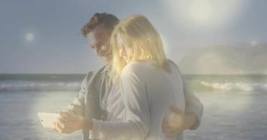 Okyanus kıyısına yaslanan çiftler, tablet üzerinde teknolojiyi incelerken güneş ışığı yavaşça kayıyor. Romantizm, bağlantı, dinginlik, açık hava, eğlence, teknoloji, doğal