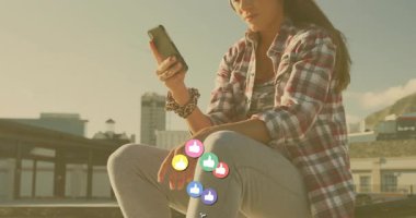 Çatıda akıllı telefonları dinleyen bir kadın sosyal medya dalgalanmasını gösteren başparmak kaldıran ikonlar görüyor. Teknoloji, iletişim, sosyal, canlı, modern, kentsel, dijital