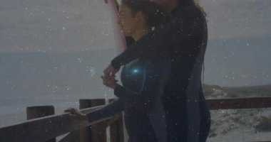 Güneş ışığı merceklerin parlamasına neden olur, erkeğin okyanusa bakan kadını kucaklaması sörf tahtasının yanında seyahat anını paylaşması. Romantizm, bağlantı, eğlence, açık hava, macera, sükunet, sahil