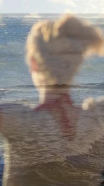 Bir kadının saçını gevşetip kollarını kaldırırken ön planda dalgalarla sahile bakan bir kadının dijital bileşimi.