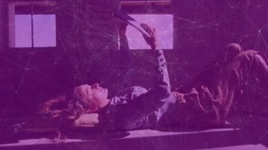 Ahşap zeminde uzanan kadın tablete uzanan yastık kullanıyor ve pencere ışığında kitap okuyarak öğreniyor. Rahatlama, konsantrasyon, farkındalık, rahatlık, minimalist, doğal ışık, konforlu