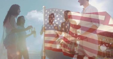 Arkadaşlar bira şişelerini geçirip bayrak sallayarak sahilde ızgaranın yanında tost yapıyorlar. Kutlama, yoldaşlık, açık hava, rahatlama, canlı, sosyal, boş zaman