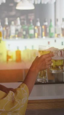 Animation of glass with beer over diverse friends having drink in bar. Leisure, free time and celebration concept digitally generated video.