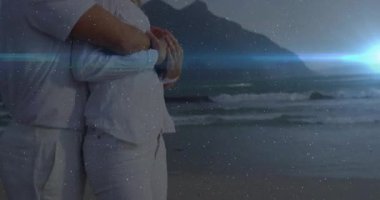 Kamera, günbatımı plajında kalp ikonu ile sarılan kadın ve erkeği gösteriyor. Romantizm, samimiyet, şefkat, manzara, huzur, uyum, rahatlık