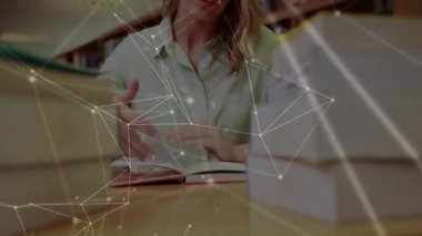 Kadın kütüphane çalışmasında öne doğru uzanıyor ve içeriği okurken sayfaları çeviriyor. Edebiyat, konsantrasyon, öğrenim, akademik, bilgi, eğitim, yansıma