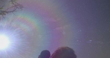 Sahildeki bankta yan yana duran çift. Gökkuşağı mercekleri parlıyor ve kamera seyahat reklamı için eğiliyor. Romantizm, dinginlik, doğa, eğlence, uyum, günbatımı, açık hava