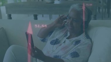 Üst düzey bir kadın, kırmızı sağlık ölçümlerini izlerken telefon ekranını dinleyip kulaklığı ayarlıyor. Teknoloji, sağlık, rahatlama, modern, yaşlı, dijital, sağlık izleme