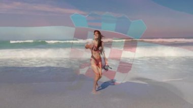 Sahile çıkan bir kadın bikini üstünden tişört çekiyor, sarong çeviriyor, seyahat reklamı için dalgalara giriyor. Plaj, kıyı şeridi, yaz, rahatlama, tasasız, ufukta akış