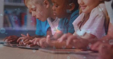 Çocuklar tabletleri masaya yerleştirir, simgeleri tıklatır ve kaydırır, uygulama etkileşimlerini başlatır. Eğitim, teknoloji, sınıf, gençlik, dijital, etkileşim, yenilik